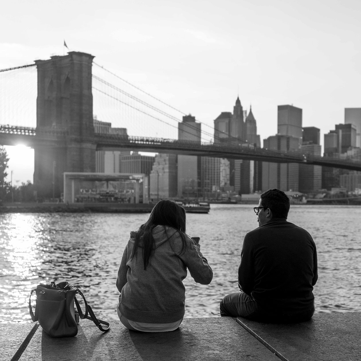 a couple sits in the park, near the Brooklyn Bridge