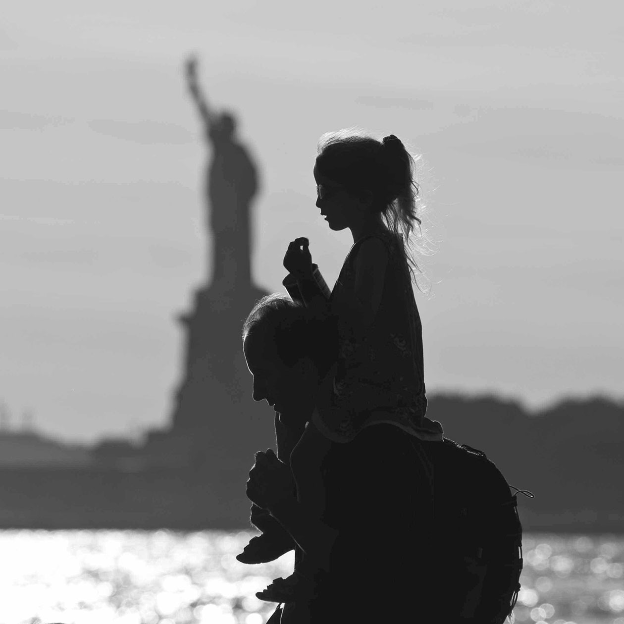 daughter on father's shoulders with Statue of Liberty in background