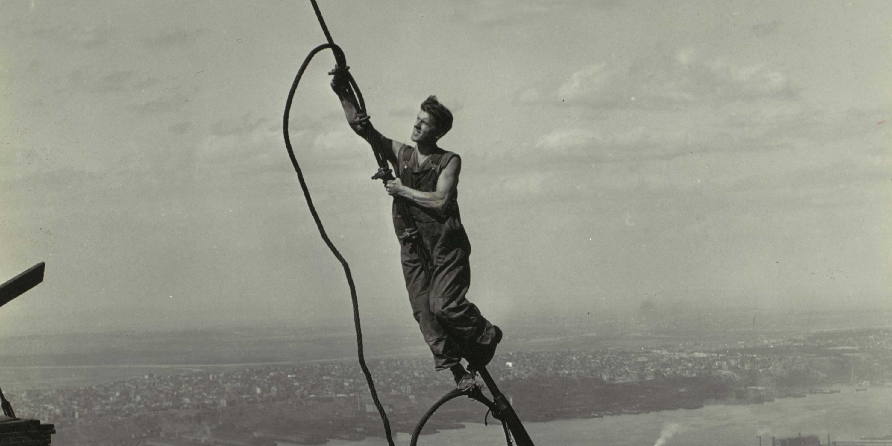 construction worker hangs on wire while building the Empire State Building