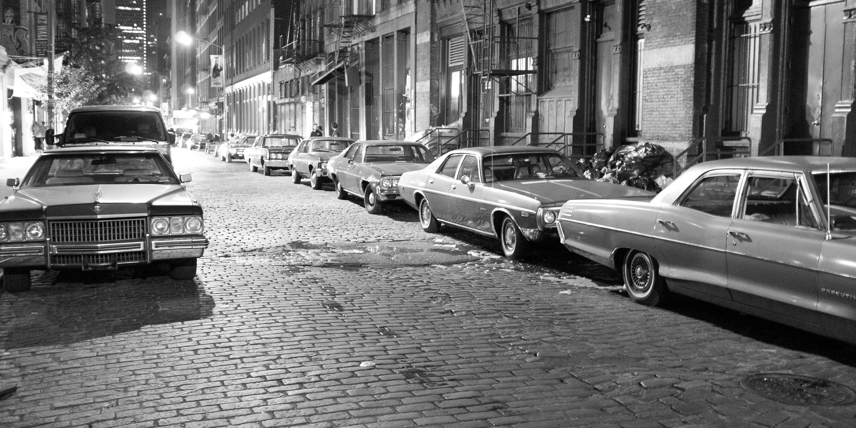 SoHo street at night, lined with cars from 1970's, part of a movie shoot